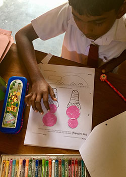 A young Sri Lankan boy works on a worksheet with pictures of ice-cream cones.