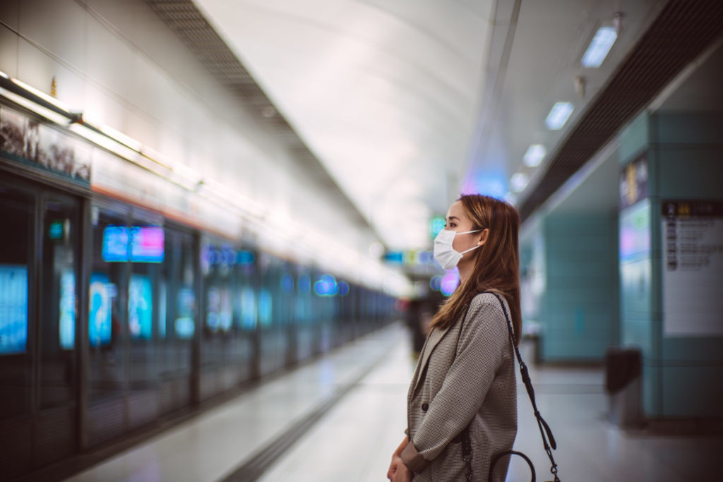 Young Asian woman with protective face mask commuting in the city and waiting for train in platform